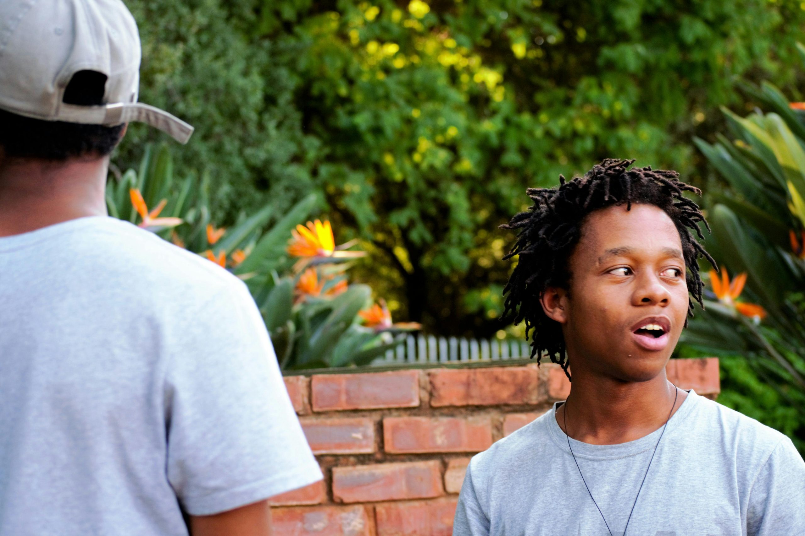 Two young adults engage in conversation outdoors, framed by lush greenery and vibrant flowers.